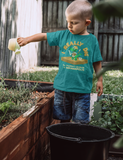 child watering a raised bed garden, wearing the I Really Dig The Children's Museum of Indianapolis shirt.