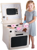 Young girl holding a tray of pretend baked goods, standing next to the bake shoppe chair cover playset.  