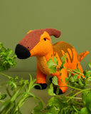 Orange knit parasaurolophus in a green room surrounded by stalks of parsley as if in a forest or field.