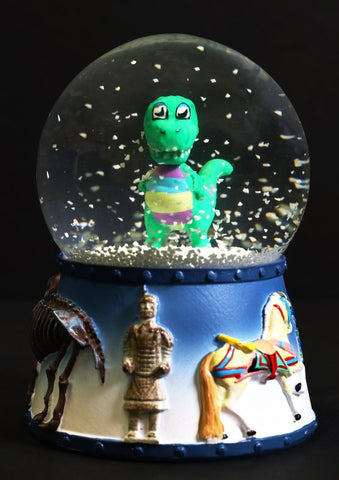 Cute dinosaur Rex inside a snowglobe with a 3-D base where you can see a Terra Cotta Warrior, a Carousel horse, and part of a Mammoth skeleton.