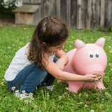 Young child 'feeding' grass to her Pink Pig Farm Hopper in the yard.