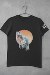 Dark charcoal grey tee shirt on hanger in front of a grey, concrete looking wall.  The Children's Museum logo is partially visible in white on the left sleeve.  The main design on the front is an Allosaurus charging forward, mouth roaring.  There is a reddish-brown circle behind it to look like sky and earth.